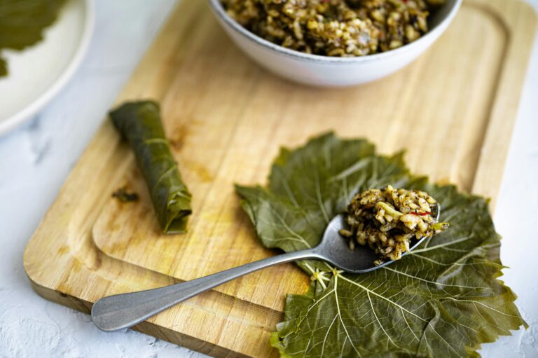 Top view of dolma yalanji preparation on a wooden board with grape leaves.