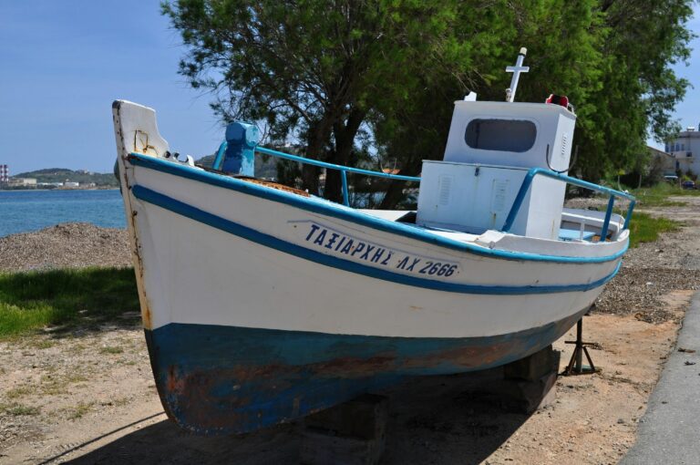 A classic Greek fishing boat on the shore of Chios, Greece under a clear sky.